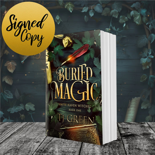 Book titled 'Buried Magic' by T.J. Green with a signed copy label on a wooden surface with leaves. Witch Fiction, magic, books about witches.