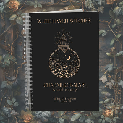 Black notebook with gold design and text on a decorative background with plants and flowers.