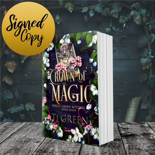 Book titled 'Crown of Magic' by TJ Green with a floral design on a wooden surface and leafy background. Book about witches, fiction, Beltane, White Haven Witches