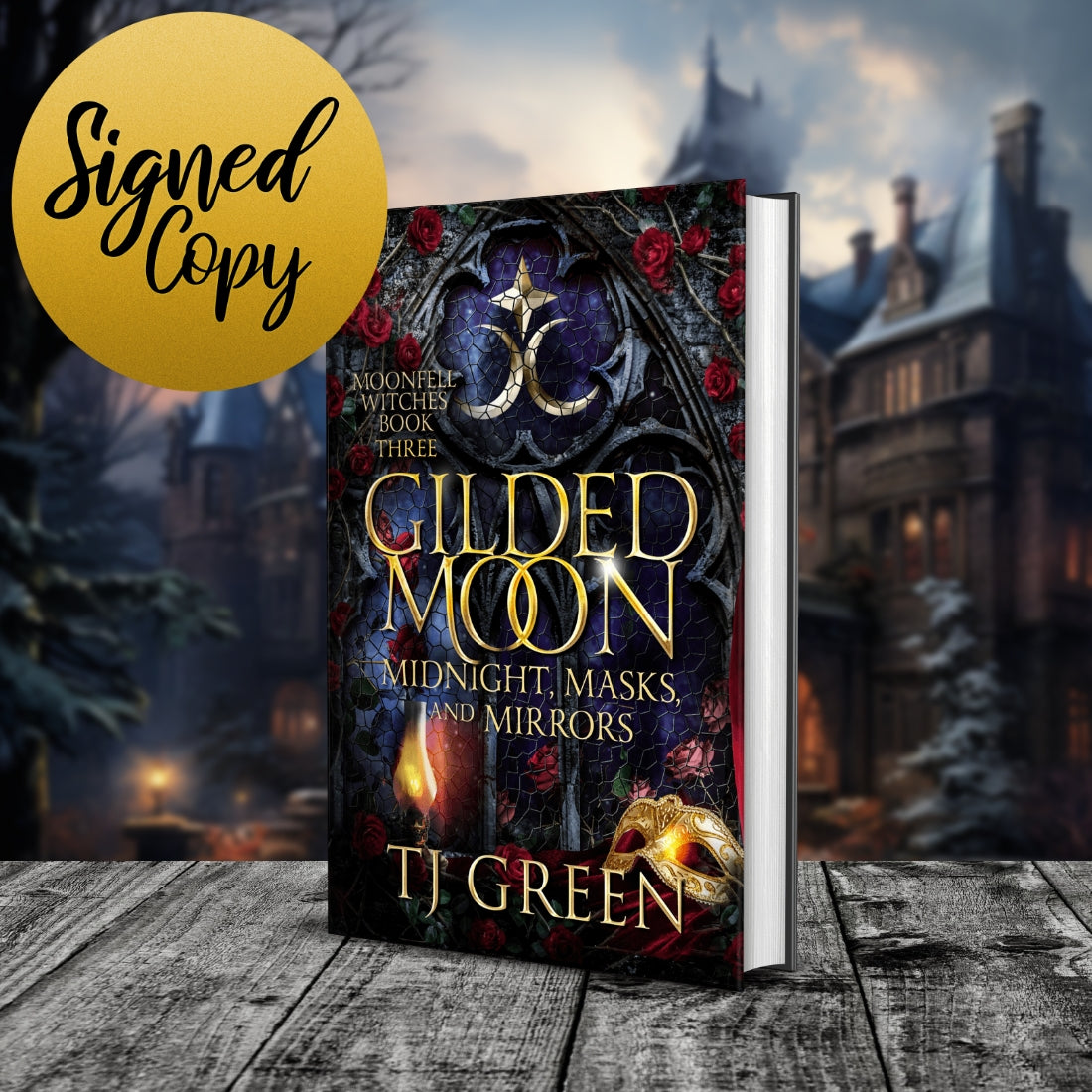 Book cover for 'Gilded Moon' by TJ Green, shown as a 3D mockup standing on a wooden surface with a blurred gothic village background. A gold circular badge in the top-left corner reads 'Signed Copy'.