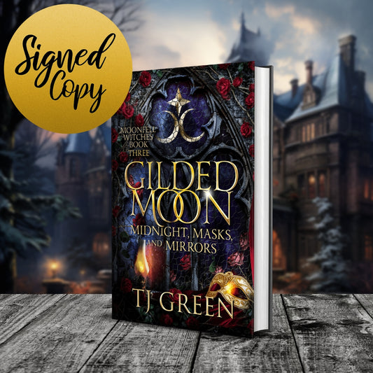 Book cover for 'Gilded Moon' by TJ Green, shown as a 3D mockup standing on a wooden surface with a blurred gothic village background. A gold circular badge in the top-left corner reads 'Signed Copy'.