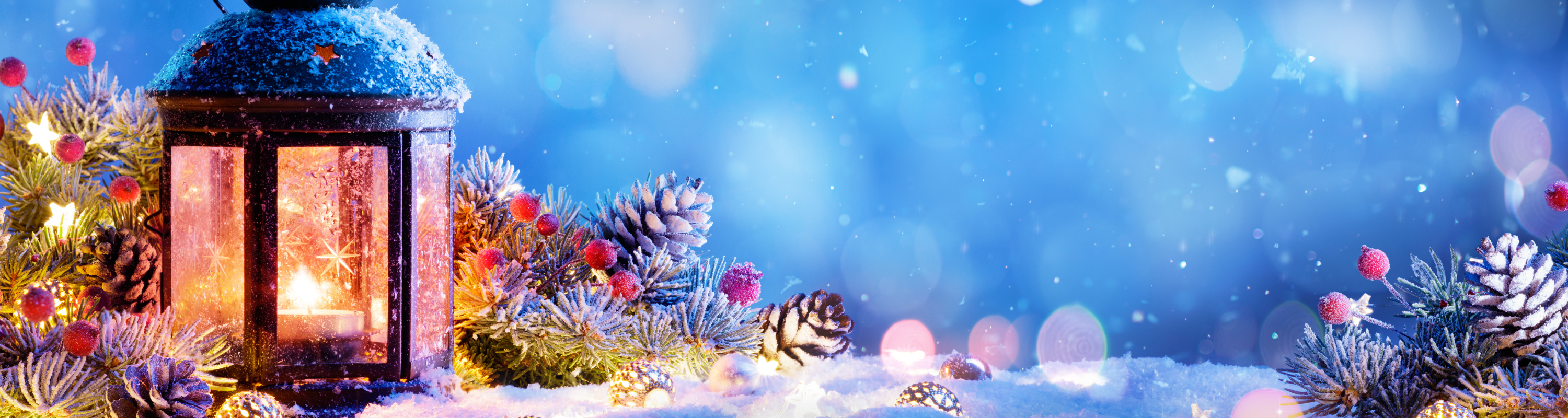 Lantern with candles surrounded by pine cones, berries and snow.