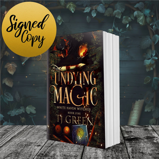 Book titled 'Undying Magic' by T.J. Green with a signed copy label on a wooden surface and leafy background. Books about witches, Cornish myths, vampires