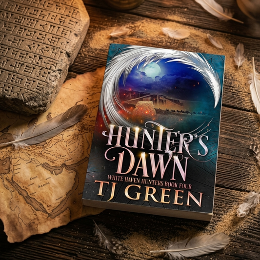 A book titled "Hunter's Dawn" by TJ Green lies on a rustic wooden surface surrounded by feathers, a stone tablet, and an old map. The cover art shows a dark fantasy scene with a glowing moon and swirling white and blue light.